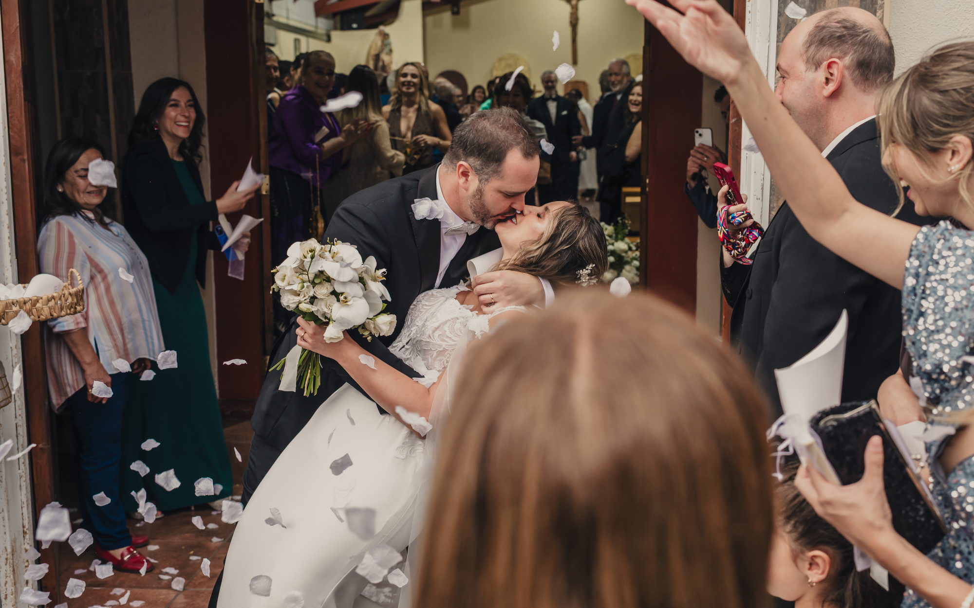 Couple kissing as they leave the church among falling petals
